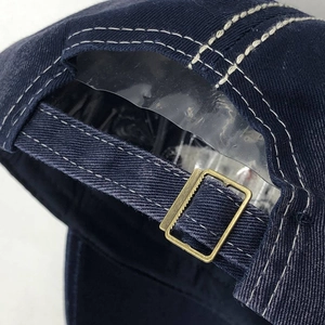 Detail of navy cotton baseball cap with adjustable brass buckle and white stitching