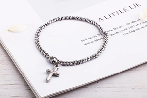 Detail of silver box chain bracelet with textured cross pendant on white book background