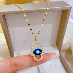 Gold Hamsa Hand necklace with blue Evil Eye and small zircons on a delicate water wave chain