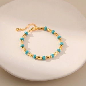 Vintage style gold and turquoise beaded bracelet displayed on a white ceramic plate