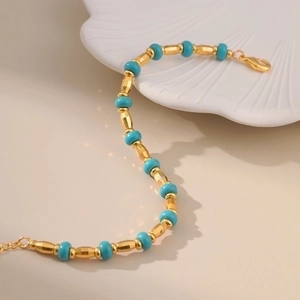 Handmade turquoise bead bracelet with gold accents on a white shell plate