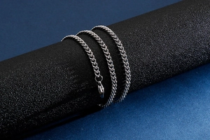 Close-up of a silver stainless steel chain link necklace wrapped on a black display stand