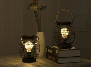 Detail of black metal wire cage lanterns with copper wire LED lights on a wooden table
