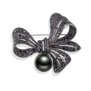 Vintage bow brooch with black rhinestones and a large polished pearl on white background