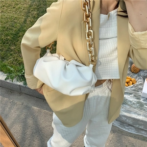 Fashionable white cloud bag with chunky gold chain strap shown on a model outdoors