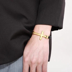 Close-up of golden cross charm on black braided leather bracelet worn on wrist