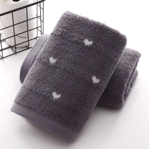 Deep grey cotton towel with white heart pattern stacked neatly by a black basket