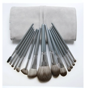 Flat lay of 12 gray makeup brushes with pearlized handles and storage bag on white backdrop