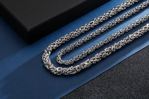 Detailed close-up of woven stainless steel dragon bone chain necklaces on blue surface