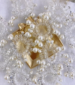 Dettaglio di elastici per capelli a spirale trasparenti con perle su una scatola oro