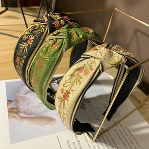 Vintage embroidered knotted headband with floral patterns on a display stand