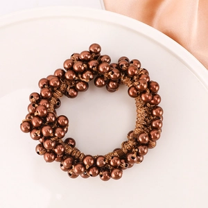 Brown beaded elastic hair tie with metallic finish pearls on a white tray background