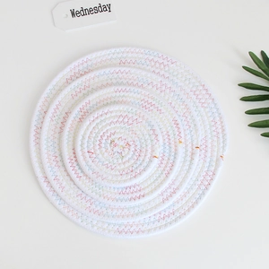 Close-up of three stacked white woven cotton coasters with colorful stitching and green leaf