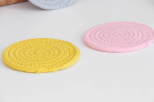 Detail of round woven cotton rope coasters in yellow and pink with spiral texture