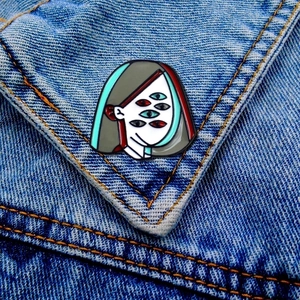 Detail of surreal enamel brooch with multiple eyes pinned on a blue denim jacket