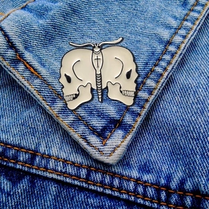 Detail of a butterfly enamel pin with skull motif on a blue denim jacket pocket