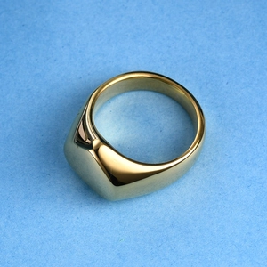Top-down view of polished gold signet heart ring on a textured blue background surface
