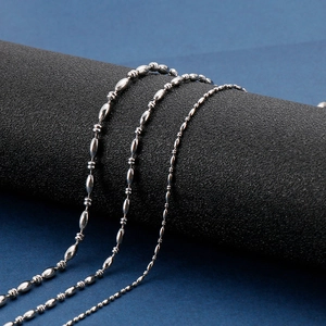 Three assorted silver stainless steel bead and link chains for men displayed on a dark pillar