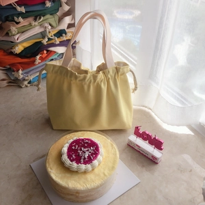 Detail of yellow canvas drawstring tote bag with white handles and colorful background