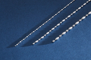 Detail of silver stainless steel bead chain with textured bamboo links on blue background