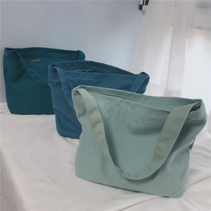 Detailed view of canvas tote bags in deep green, medium blue, and light bean green colors