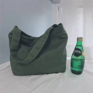 Detail of dark green canvas tote bag with wide strap next to a glass bottle for size