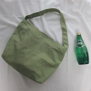 Detail view of a green canvas shoulder bag on white textured fabric with a green bottle