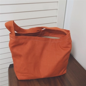 Close-up of bright orange canvas tote bag with zipper closure on dark wooden table