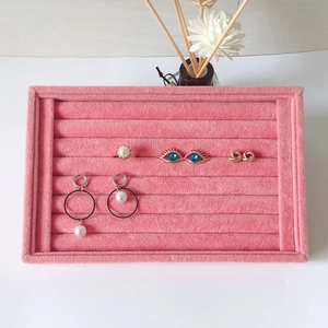 Pink velvet jewelry display tray with various rings and earrings on a white surface