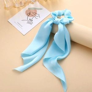 Close-up of a light blue satin ribbon hair tie on a beige cylindrical display stand