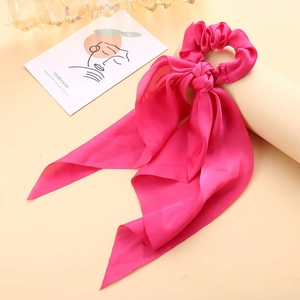 Detail of rose red satin bow hair scrunchie with long ribbons on a white prop stand