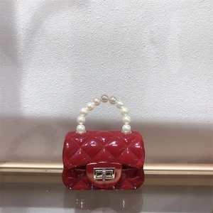 Detail of a red mini jelly bag with quilted texture, pearl handle and turn-lock closure