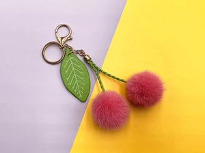Detail of pink plush cherry keychain with green leather leaf and golden metal clasp