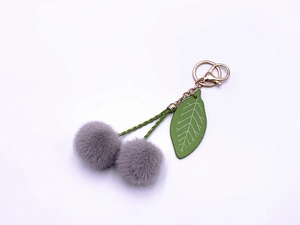Close-up of grey fluffy cherry keychain with green leaf and golden metal clasp