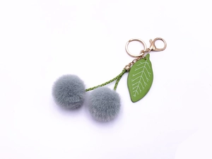 Detailed close-up of grey faux fur cherry keychain with green leaf and golden metal clasp