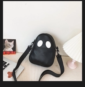 Detail of cute ghost-shaped black PU crossbody bag on a textured desk with lifestyle decor