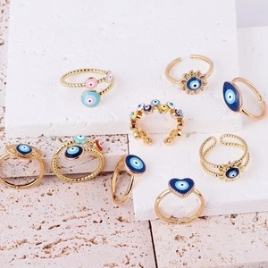 Set of gold adjustable evil eye rings with colorful enamel details on stone background