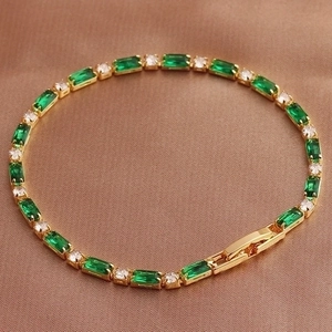 Detail of a golden bracelet with green emerald-cut and clear round cubic zirconia stones