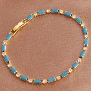 Detailed view of golden bracelet with blue rectangular gems on brown silk background