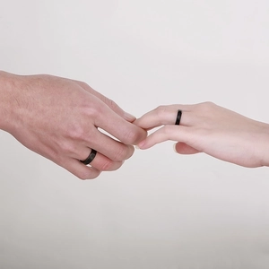Close-up of minimalist black couple rings on hands over a soft beige background
