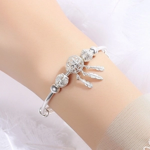 Dreamcatcher silver bangle with intricate feather charms and hollow orb on white feathers