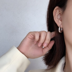 Macro shot of minimalist silver C-shaped chunky hoop earrings worn by a model