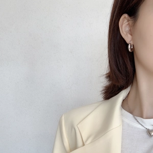Close-up of minimalist silver C-shaped hoop earrings and heart pendant on a model
