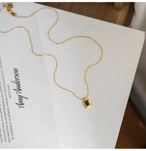 Elegant gold necklace with emerald green gemstone pendant on minimalist background