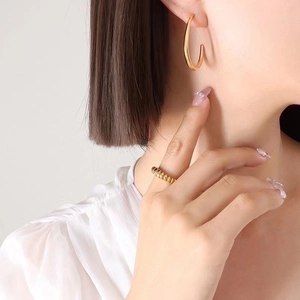 Macro shot of minimalist gold C-shaped earrings and textured ring on female model