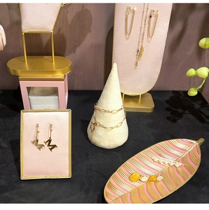 Detail of gold jewelry collection with Dior earrings and pearl hair clips on pink stand
