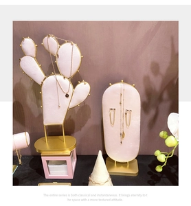 Pink velvet cactus and oval jewelry stands with gold metal frames on dark background