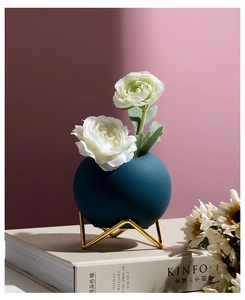 Detail of dark blue matte ceramic vase with golden metal base and white faux flowers