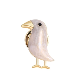Detail of bird brooch with white enamel inlay, gold metal frame, and black rhinestone eye