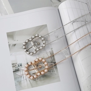 Elegant gold and silver chain belts with oval pearl buckles on a fashion magazine background
